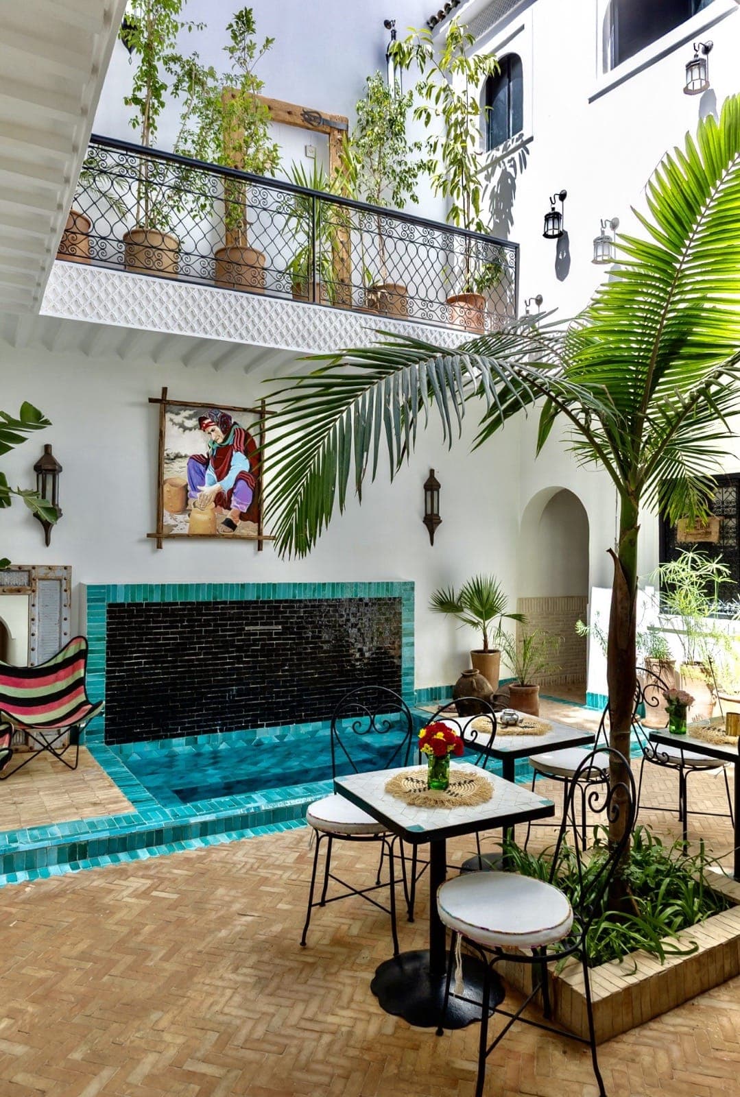 The courtyard of Riad Taww'Ami - a turquoise plunge pool under the balcony, lanterns and palms